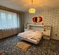 Ložnice v rodinném domě s květinovým kobercem a velkým oknem.