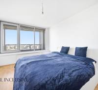 Ložnice v 2pokojovém bytě s postelí a velkým oknem, podlaha s dřevěným dekorem.