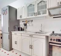 Kuchyně v 3-pokojovém bytě s bílými skříňkami, sporákem a velkou lednicí.