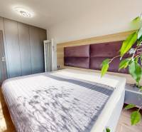 Ložnice ve 3-pokojovém bytě s podlahou s dřevěným dekorem, velkou postelí a rostlinou.