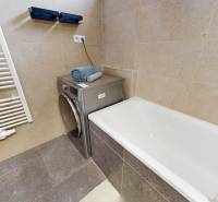 Koupelna v 3-pokojovém bytě s vanou, pračkou a ručníky na béžových obkladech.