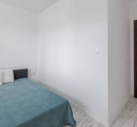 Ložnice v dvoupokojovém bytě s postelí, polštáři a dřevěnými dveřmi.