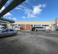 Sklady a haly v Nových Zámcích na ulici Nové Zámky s průmyslovým komplexem a auty.