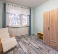 Pokoj ve 4pokojovém bytě se skříní, křeslem a podlahou s dřevěným dekorem.