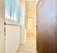 Chodba s podlahou s dřevěným dekorem, bílé stěny, velké okno se žaluziemi.