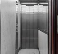 Šedý výťah s kovovou kabínou a ovládacím panelom.