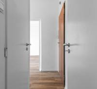 Biely interiér 1-izbového bytu s podlahou s dreveným dekorom a otvorenými dverami.