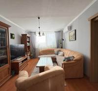 Obývací pokoj s pohodlnou sedačkou, podlahou s dřevěným dekorem a příjemným osvětlením ve 3-pokojovém bytě.