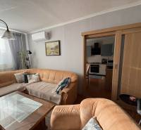 Obývací pokoj s pohovkou, skleněným stolem a kuchyní ve 3pokojovém bytě.