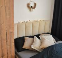 Ložnice v 3pokojovém bytě s dekorativním věncem a černými závěsy; postel s polštáři.