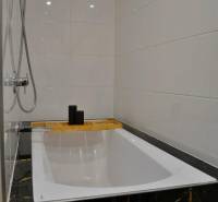 Koupelna v 3-pokojovém bytě s vanou, sprchovou hlavicí a bílými obklady.