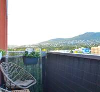 Balkon s ratanovými křesly a výhledem na zeleň ve 3-pokojovém bytě.