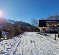 Sněhem pokrytá cesta před chatou na ulici v Mýtě pod Ďumbierom, za slunečného zimního dne.