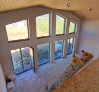 Interiér chaty s velkými okny, schody a podlahou s dřevěným dekorem.