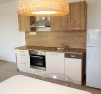 Kuchyně v garsonce na ulici Bodona s dřevěnými skříňkami, sporákem a lednicí.