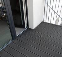 Balkon s dřevěnou podlahou na ulici Bodona, součást garsonky s velkým oknem.