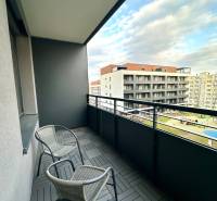 Balkon se dvěma židlemi a dlaždicemi s dřevěným dekorem, výhled na budovy.