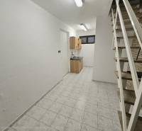 Interiér s bílými stěnami, kuchyňskou skříňkou, schodištěm a podlahou s dřevěným dekorem.