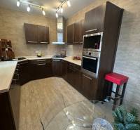 Kuchyně v rodinném domě s dřevěným dekorem podlahy a bohatým osvětlením.