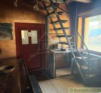 Interiér rodinného domu s kovovým schodištěm a dřevěným stolem, světlé stěny.