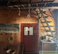 Interiér rodinného domu s dřevěnými schody, rustikálním stolem a uměleckou malbou na stěně.