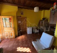 Pokoj v rodinném domě s cihlovou podlahou, dřevěným stropem a žlutými stěnami.