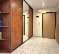 Vstupní chodba v 2-pokojovém bytě s dlažbou a policemi s knihami.