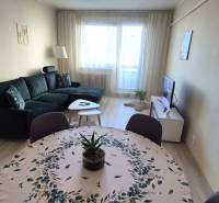 Obývací pokoj s tmavou sedačkou, jídelním stolem a podlahou s dřevěným dekorem v 2pokojovém bytě.