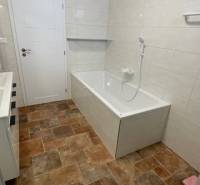 Koupelna v rodinném domě má vanu, bílé obklady, podlahu s dřevěným dekorem.