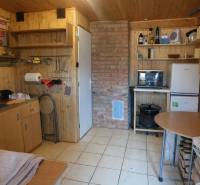 Kuchyňka v chatě s dřevěným dekorem a cihlovým komínem, vybavená základním nábytkem.