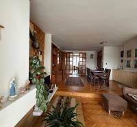 Obývací pokoj v rodinném domě s podlahou s dřevěným dekorem, jídelním stolem a křížem na stěně.