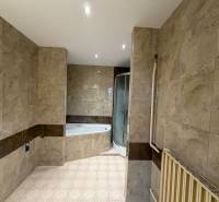 Koupelna v rodinném domě s obkladem mramorového vzhledu a rohovou vanou.