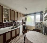 Kuchyně v rodinném domě s dřevěnými skříňkami, kulatým stolem a podlahou s dřevěným dekorem.