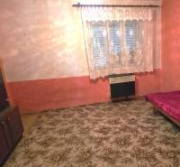 Pokoj v rodinném domě s kobercem, postelí a skříňkou, záclonou na okně.