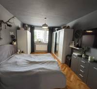 Ložnice v 3-pokojovém bytě se skříní, postelí a podlahou s dřevěným dekorem.