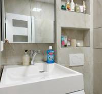 Koupelnový prostor garsonky s umyvadlem, zrcadlem a vestavěnými poličkami s kosmetikou.