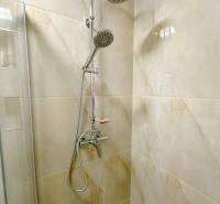 Sprchový kout s keramickými obklady a dešťovou sprchou v garsonce.