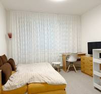 Garsonka s postelí, pracovním stolem, televizí a záclonami na okně.