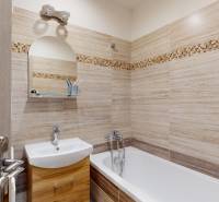 Koupelna v 2-pokojovém bytě se světlými obklady a vanou, skříňky pod umyvadlem.