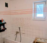 Koupelna v rodinném domě s vanou, poličkou a bílými kachličkami.