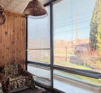 Rodinný dům s ratanovou lampou, křeslem s dekou a okny se žaluziemi.