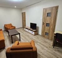 Obývací pokoj v 2-pokojovém bytě s oranžovým nábytkem a podlahou s dřevěným dekorem.