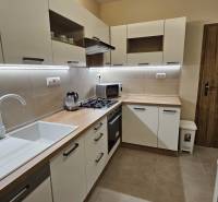 Kuchyně v 2-pokojovém bytě s bílými skříňkami a podlahou s dřevěným dekorem.