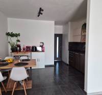 Kuchyně v 3-pokojovém bytě s jídelním stolem, tmavá podlaha a bílé židle.