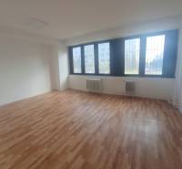 Interiér kanceláře s podlahou s dřevěným dekorem a velkými okny.