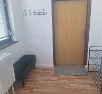 V Budově s podlahou s dřevěným dekorem je lavička, radiátor a věšák na stěně.