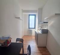 Úzká kancelář s černým stolem, židlemi a podlahou s dřevěným dekorem.