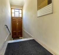 Úzké schodiště s žebříkem a lampou vede ke dřevěným dveřím. Kanceláře.