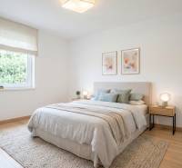 Světlá ložnice s podlahou s dřevěným dekorem, postel se světlým přehozem a obrazy na stěně.