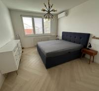 Ložnice s postelí, bílou komodou, podlahou s dřevěným dekorem a závěsným svítidlem.